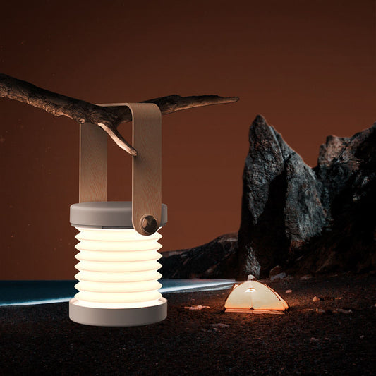 Portable foldable touch dimmable LED night light lantern hanging from a tree branch outdoors at night